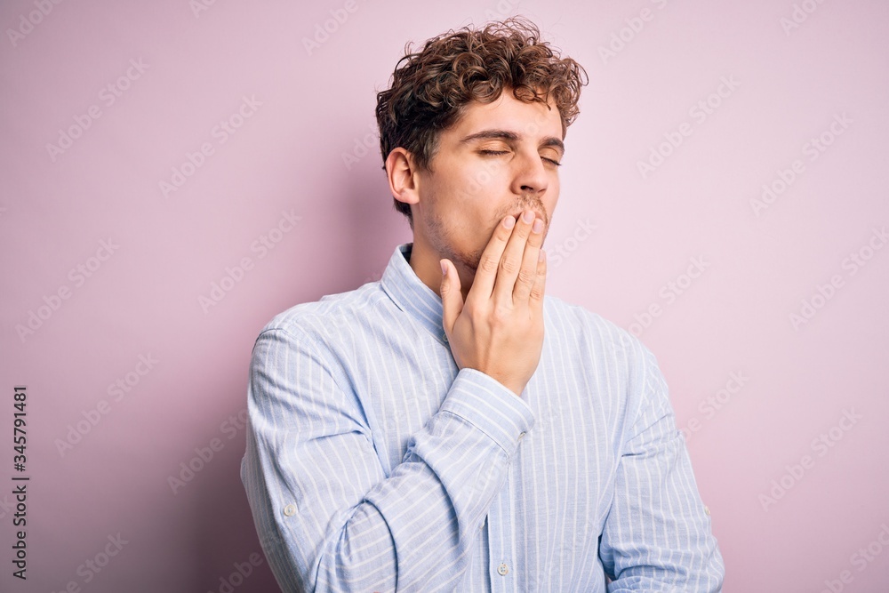 Young blond handsome man with curly hair wearing striped shirt over white background bored yawning tired covering mouth with hand. Restless and sleepiness. Young blond handsome man with curly hair wearing striped shirt over white background bored yawning tired covering mouth with hand. Restless and sleepiness.