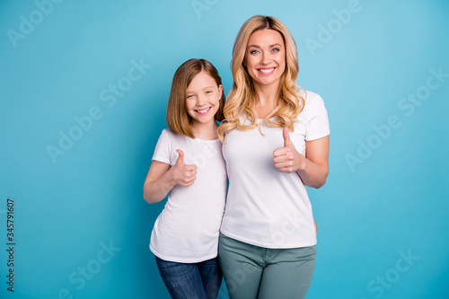 Photo of two people attractive mommy lady little daughter hold thumb fingers raised up express agreement cheerful person wear casual white s-shirts isolated blue color background