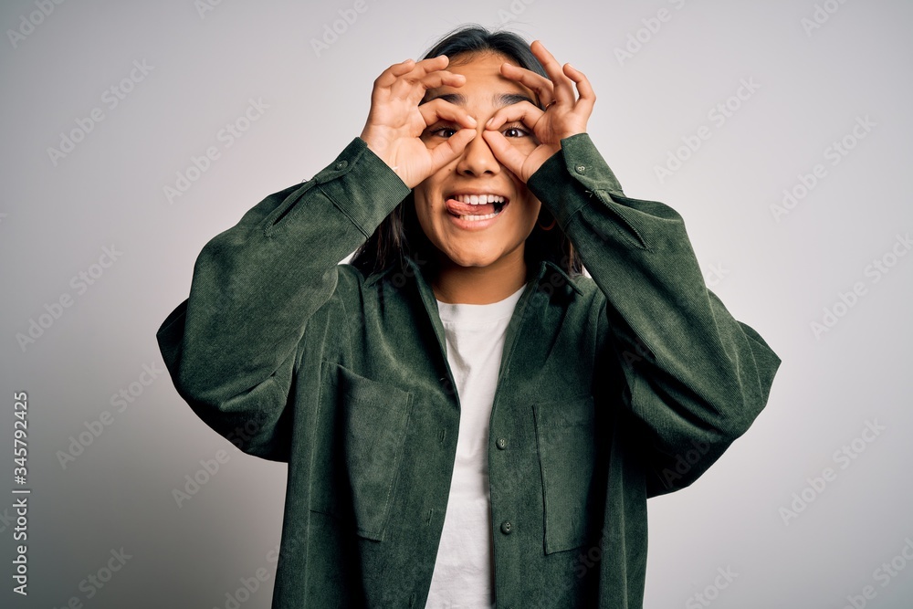 Young beautiful asian woman wearing casual shirt standing over isolated white background doing ok gesture like binoculars sticking tongue out, eyes looking through fingers. Crazy expression. Young beautiful asian woman wearing casual shirt standing over isolated white background doing ok gesture like binoculars sticking tongue out, eyes looking through fingers. Crazy expression.