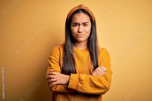 Young beautiful asian woman wearing casual sweater and diadem over yellow background skeptic and nervous, disapproving expression on face with crossed arms. Negative person. © Krakenimages.com
