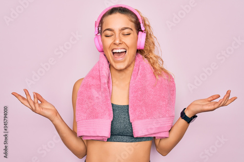 Konstfotografi Young beautiful sporty woman with blue eyes wearing towel listening to music using headphones celebrating mad and crazy for success with arms raised and closed eyes screaming excited