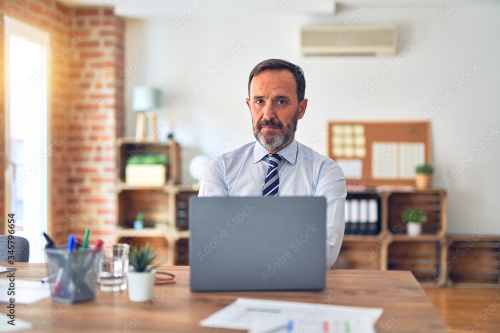 Middle age handsome businessman wearing tie sitting using laptop at the office skeptic and nervous, disapproving expression on face with crossed arms. Negative person. Middle age handsome businessman wearing tie sitting using laptop at the office skeptic and nervous, disapproving expression on face with crossed arms. Negative person.