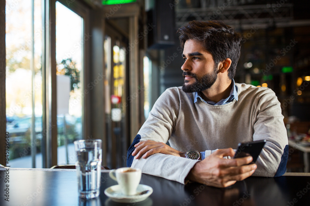 Handsome young bearded man in cafe use phone while waiting someone Handsome young bearded man in cafe use phone while waiting someone