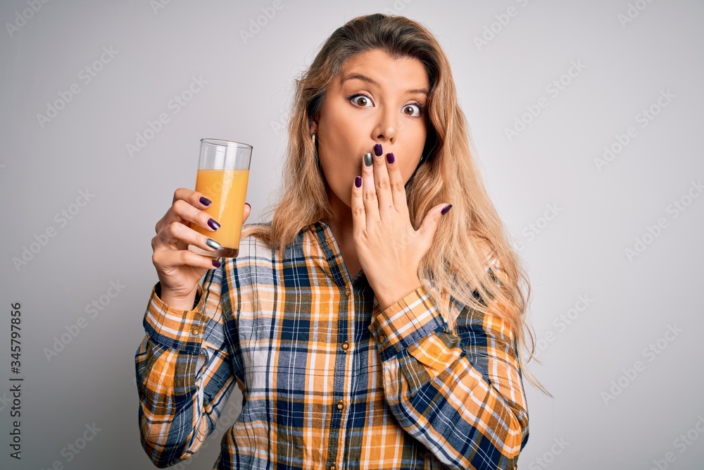Young beautiful blonde woman drinking glass of healthy orange juice over white background cover mouth with hand shocked with shame for mistake, expression of fear, scared in silence, secret concept Young beautiful blonde woman drinking glass of healthy orange juice over white background cover mouth with hand shocked with shame for mistake, expression of fear, scared in silence, secret concept
