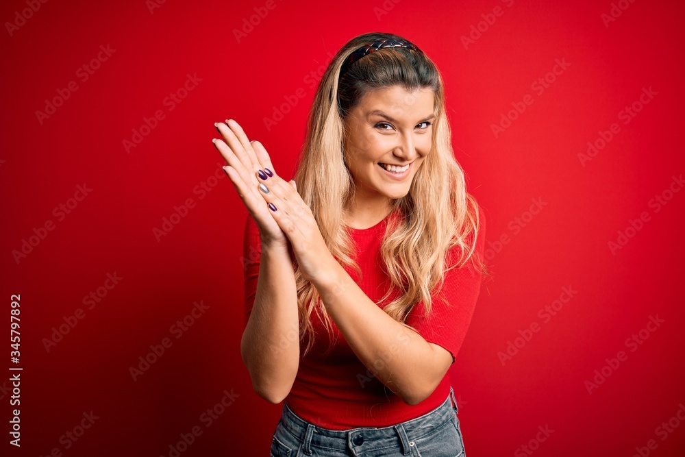 Young beautiful blonde woman wearing casual t-shirt standing over isolated red background clapping and applauding happy and joyful, smiling proud hands together Young beautiful blonde woman wearing casual t-shirt standing over isolated red background clapping and applauding happy and joyful, smiling proud hands together