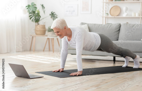 Active Senior Woman Making Plank In Front Of Laptop At Home