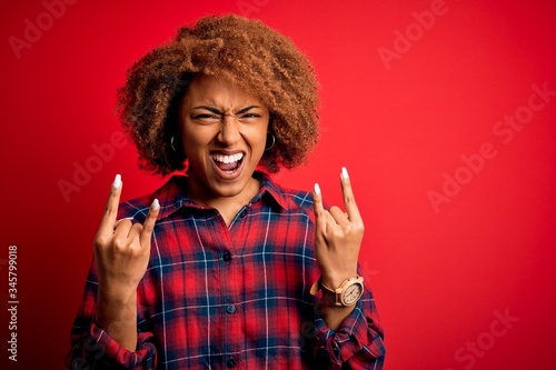 Young beautiful African American afro woman with curly hair wearing casual shirt shouting with crazy expression doing rock symbol with hands up. Music star. Heavy concept.