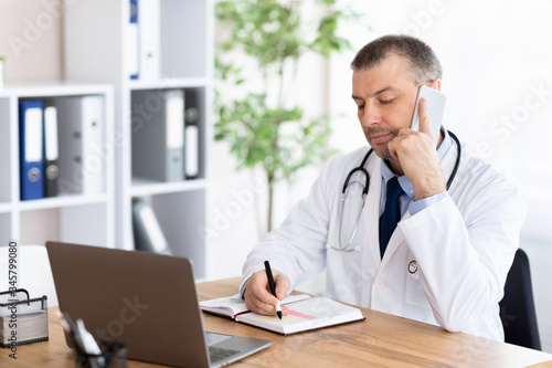 Doctor talking on phone with his patients and writing notes