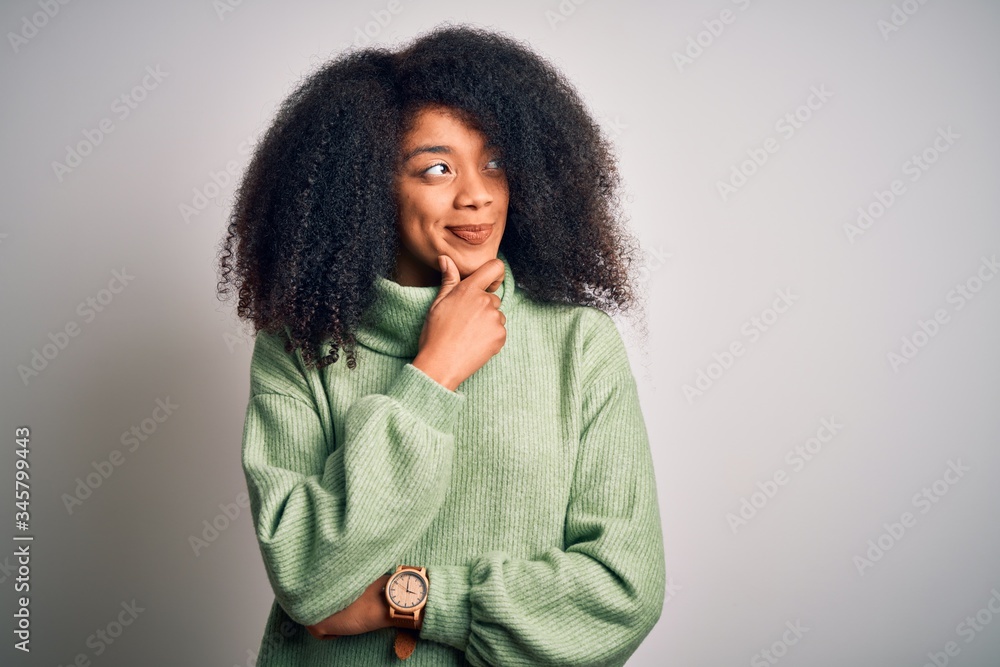 Young beautiful african american woman with afro hair wearing green winter sweater with hand on chin thinking about question, pensive expression. Smiling with thoughtful face. Doubt concept. Young beautiful african american woman with afro hair wearing green winter sweater with hand on chin thinking about question, pensive expression. Smiling with thoughtful face. Doubt concept.