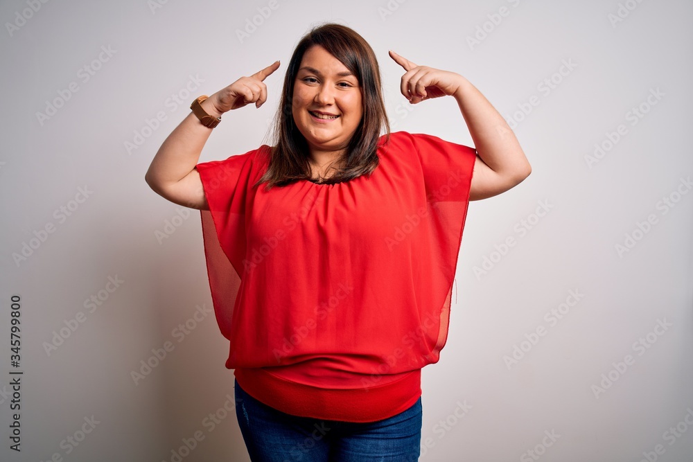 Beautiful brunette plus size woman wearing casual red t-shirt over isolated white background smiling pointing to head with both hands finger, great idea or thought, good memory