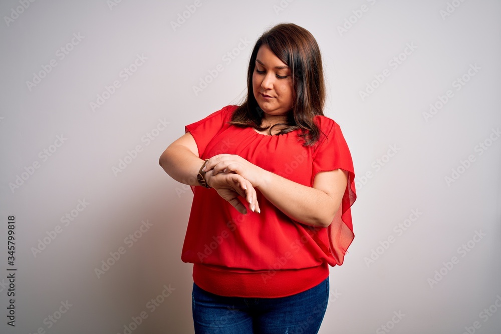 Beautiful brunette plus size woman wearing casual red t-shirt over isolated white background Checking the time on wrist watch, relaxed and confident Beautiful brunette plus size woman wearing casual red t-shirt over isolated white background Checking the time on wrist watch, relaxed and confident