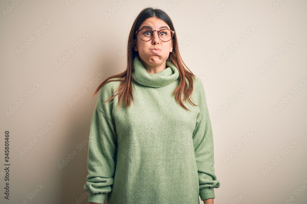 Young beautiful woman wearing casual sweater standing over isolated white background puffing cheeks with funny face. Mouth inflated with air, crazy expression. Young beautiful woman wearing casual sweater standing over isolated white background puffing cheeks with funny face. Mouth inflated with air, crazy expression.