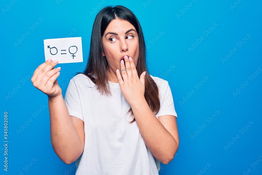 Beautiful woman asking for sex discrimination holding paper with gender equality concept covering mouth with hand, shocked and afraid for mistake. Surprised expression Beautiful woman asking for sex discrimination holding paper with gender equality concept covering mouth with hand, shocked and afraid for mistake. Surprised expression