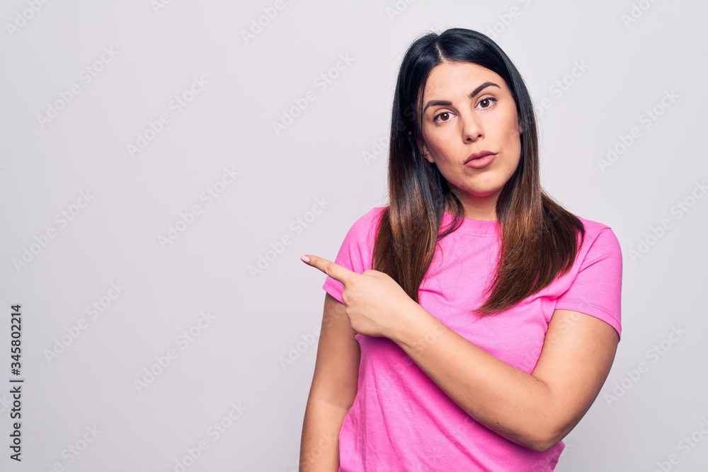 Young beautiful brunette woman wearing casual pink t-shirt standing over white background Pointing with hand finger to the side showing advertisement, serious and calm face Young beautiful brunette woman wearing casual pink t-shirt standing over white background Pointing with hand finger to the side showing advertisement, serious and calm face