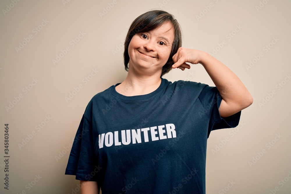 Young down syndrome volunteer woman wearing social care charity t-shirt smiling doing phone gesture with hand and fingers like talking on the telephone. Communicating concepts. Young down syndrome volunteer woman wearing social care charity t-shirt smiling doing phone gesture with hand and fingers like talking on the telephone. Communicating concepts.