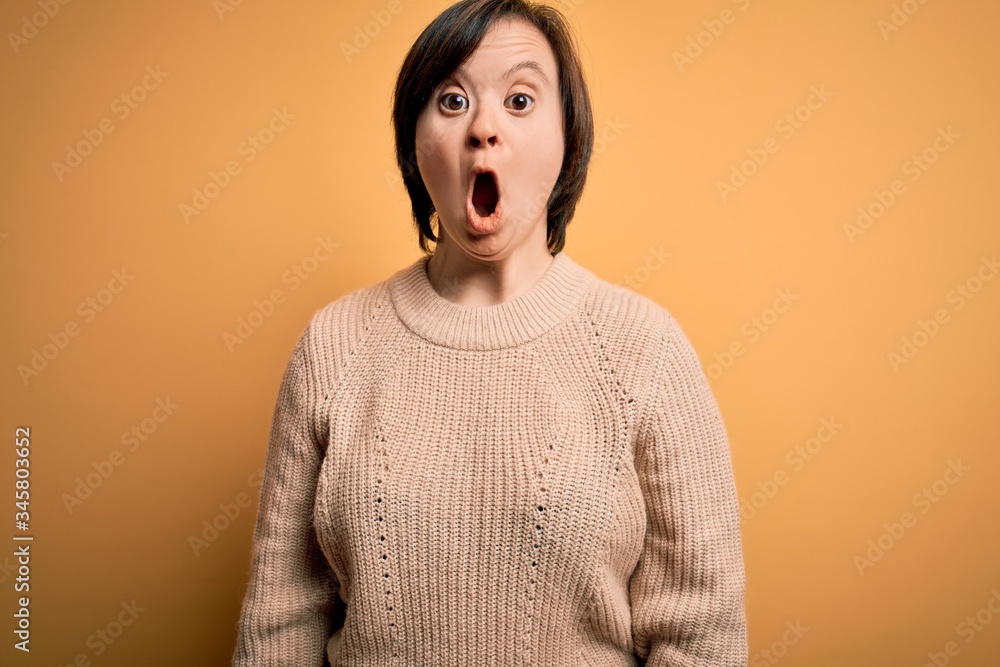 Young down syndrome woman wearing casual sweater over yellow background afraid and shocked with surprise expression, fear and excited face. Young down syndrome woman wearing casual sweater over yellow background afraid and shocked with surprise expression, fear and excited face.