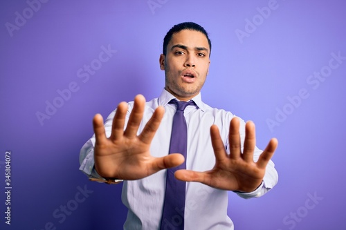 Young brazilian businessman wearing elegant tie standing over isolated purple background doing stop gesture with hands palms, angry and frustration expression © Krakenimages.com