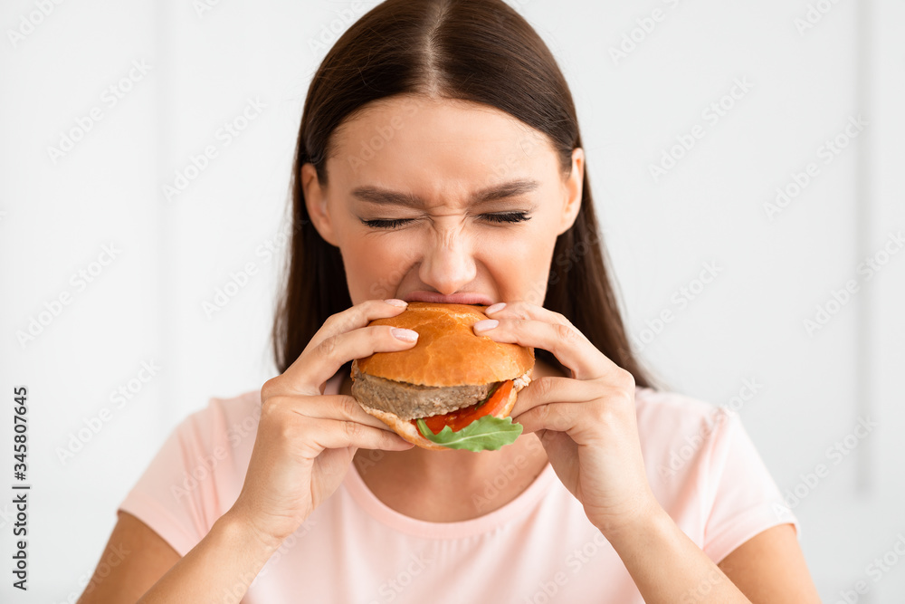 Girl Biting Burger Enjoying Junk Food Having Cheat Meal Indoors