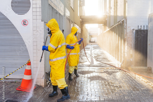 Homens de roupa de proteção amarela, fazendo a limpeza próximo aos hospitais, deivdo ao cornavirus.  Contribuem para a desinfecção das calçadas photo