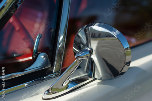 Chrome mirror of an old American muscle car. White classic car with red interior.