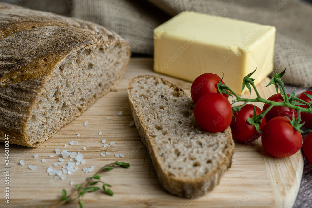 Sliced bread, butter, tomatoes, salt and herbs  on a wooden board. Color food photography.