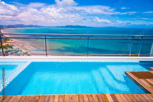 The beautiful blue swimming pool on the top roof of building with blue sea and blue cloudy sky background. 