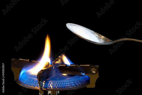 Isolated spoon with white powder over a gas burner with fire and syringe