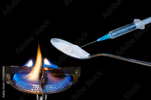 Isolated spoon with white powder over a gas burner with fire and syringe