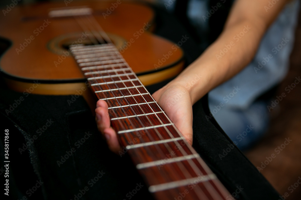 Fototapeta premium Woman observes and removes a classic brown guitar from a black case
