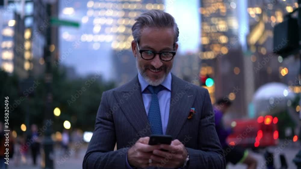 Middle aged businessman in luxury clothing using mobile phone for texting during way to office in financial district in metropolitan city, successful male proud ceo smiling during cellular messaging
