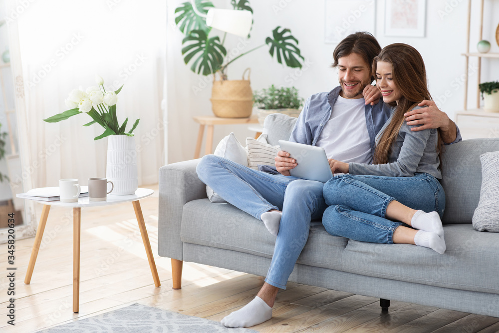Man and woman sitting on couch at home, using tablet