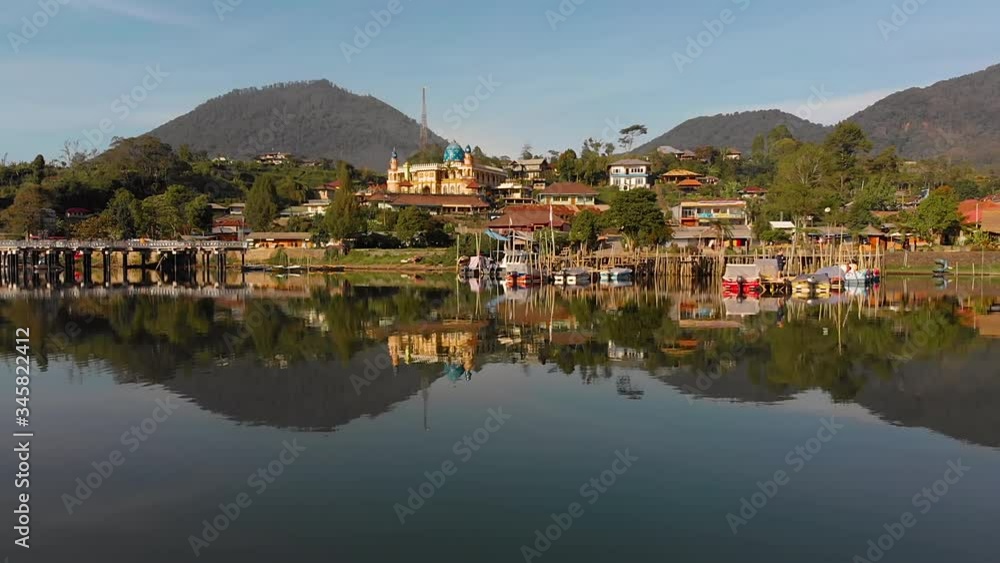 Traditional Indonesian Mosque Village at  reflective lake in morning light filmed from waterside with a drone