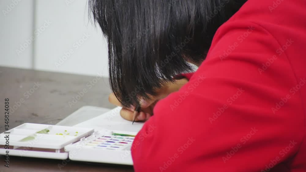 A young teenage girl is sitting and drawing and painting in a living room. A young teenage girl is sitting and drawing and painting in a living room.
