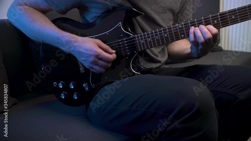 Slider shot of man practicing scales on electric guitar at home sitting on couch. photo