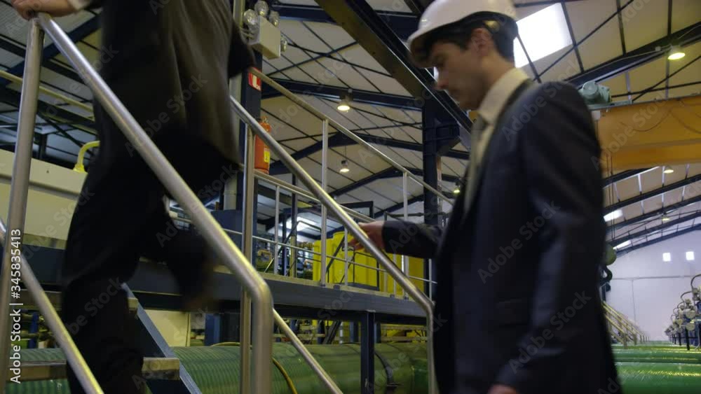 WS Two businessmen walking on gangway through industrial building WS Two businessmen walking on gangway through industrial building