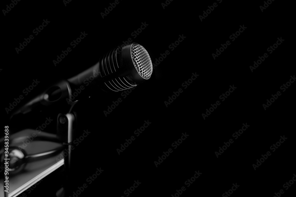 A black microphone hiding on black shadow background. Concept of recording equipment or Podcasting.