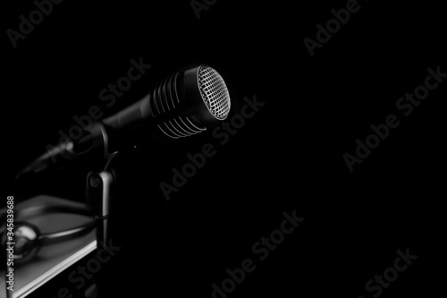 A black microphone hiding on black shadow background. Concept of recording equipment or Podcasting.