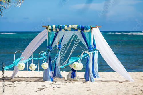 Colorful wedding arch gazebo pavilion made of bamboo and textile with fresh flowers decoration at sandy beach on sunny day for destination wedding ceremony in Dominican republic  