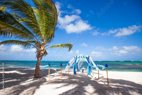 Colorful wedding arch gazebo pavilion made of bamboo and textile with fresh flowers decoration at sandy beach on sunny day for destination wedding ceremony in Dominican republic  