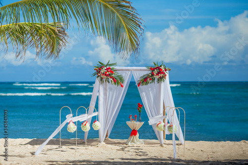 Colorful wedding arch gazebo pavilion made of bamboo and textile with fresh flowers decoration at sandy beach on sunny day for destination wedding ceremony in Dominican republic  