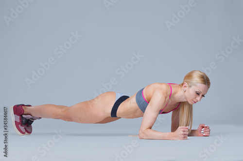 Young hardy sporty woman does plank isolated on grey background