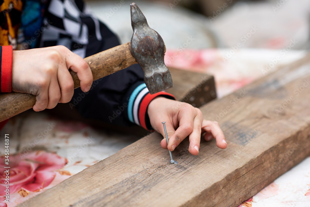 the boy’s hands are holding a hammer and hammering a nail into the board. The child repairs the boy’s hands are holding a hammer and hammering a nail into the board. The child repairs