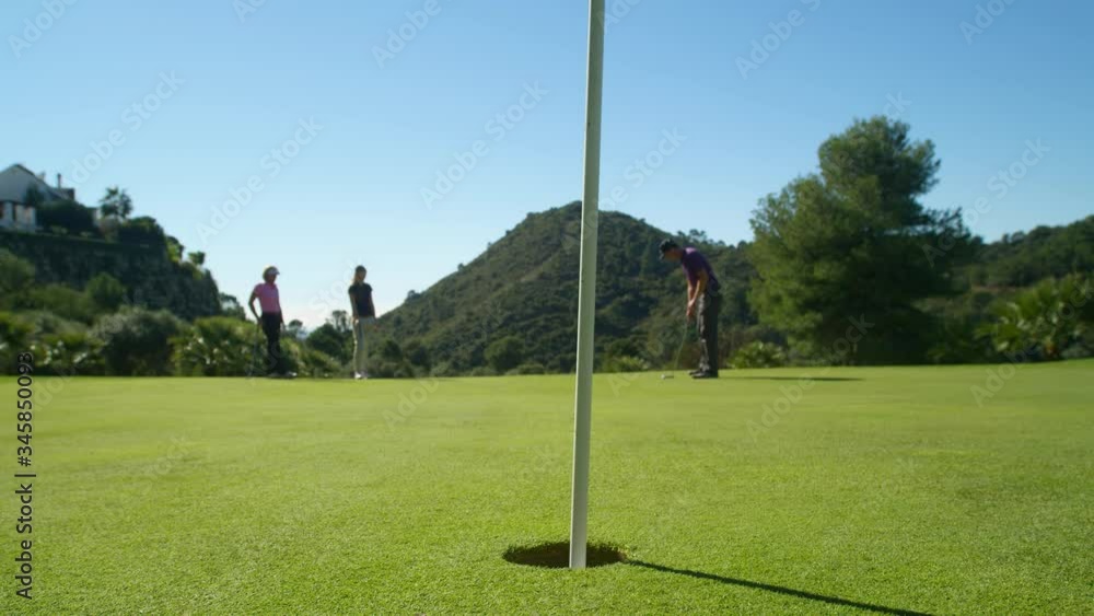 WS Three golfers on green, young golfer putting but missing WS Three golfers on green, young golfer putting but missing
