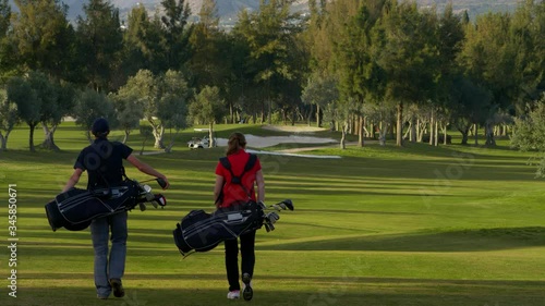 WS Young man and woman with golf bags walking along golf course fairway