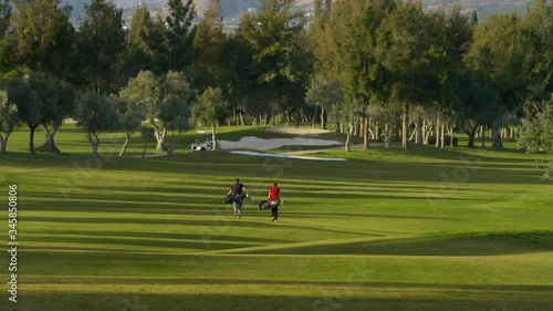 WS Young man and woman with golf bags walking along golf course fairway