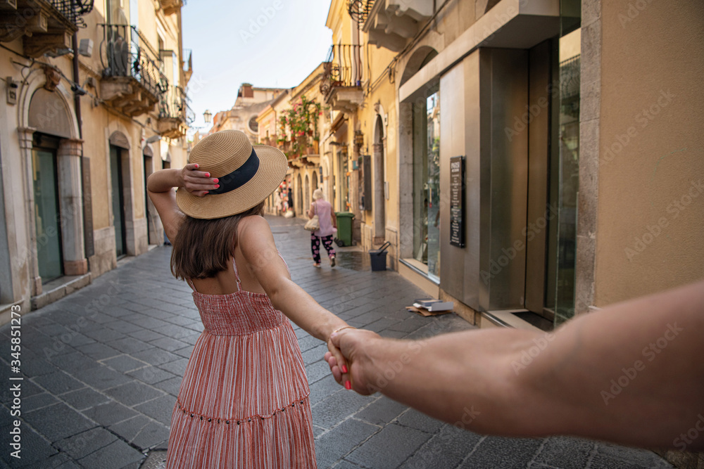 A girl and a guy are walking along European streets. A lady in a straw hat and a coral dress holds the hand of a man. Follow me challenge