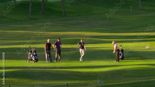 WS Four golfers on fairway, mature woman playing ball towards camera