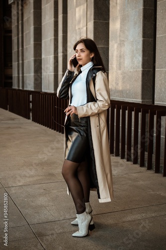 portrait Businesswoman girl in the city speaks by mobile phone. Wearing a black and white coat. Standing up