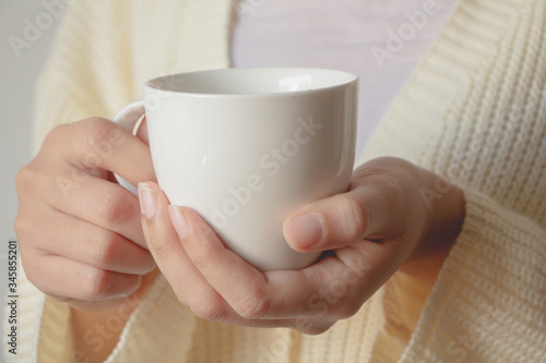 Female hand holding cup of  beverage. Beautiful girl in white sweater holding cup of tea or coffee in the morning.  