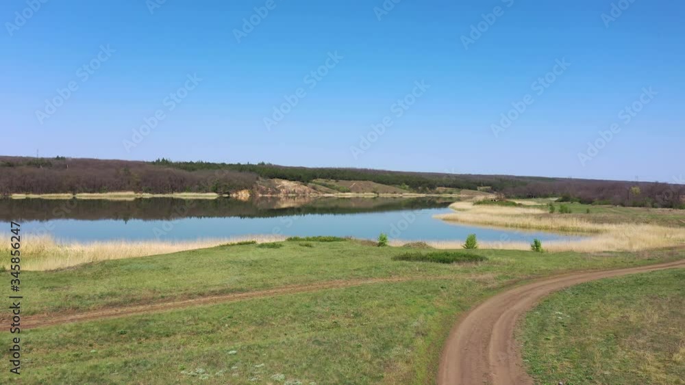 Country road near the lake. On the opposite shore of the lake is a forest. Aerial view. Spring Country road near the lake. On the opposite shore of the lake is a forest. Aerial view. Spring
